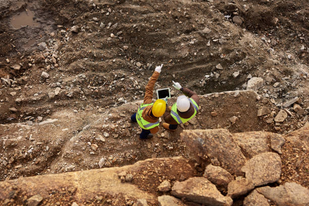 Top view shot of two industrial  workers wearing reflective jackets standing on mining worksite outdoors using digital tablet, copy space